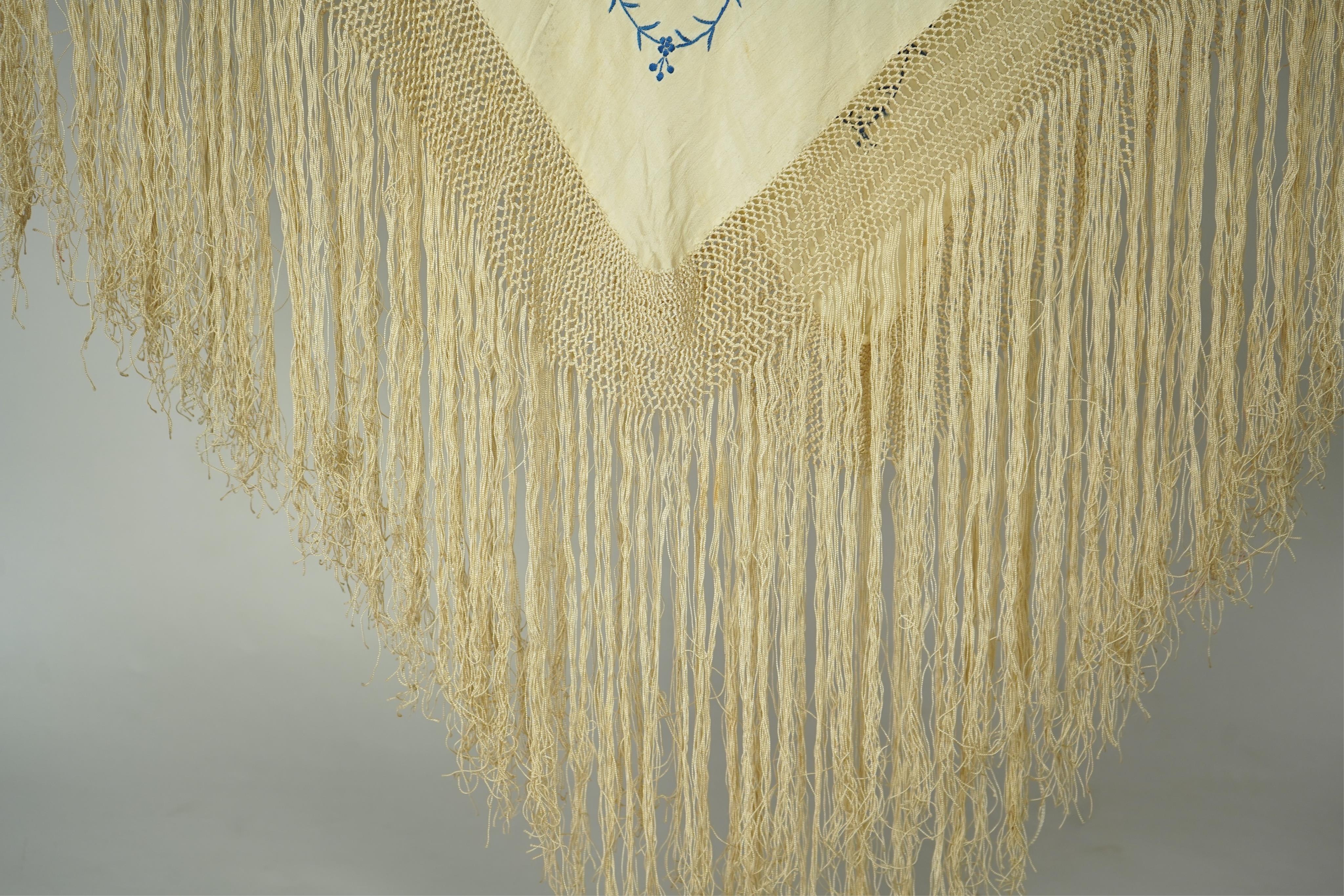 A Chinese cream silk polychrome embroidered shawl with a long fringe. Embroidered with four unusual corner cartouches of Pagoda, flowers, birds, cats and dogs. 132cm x 126cm.